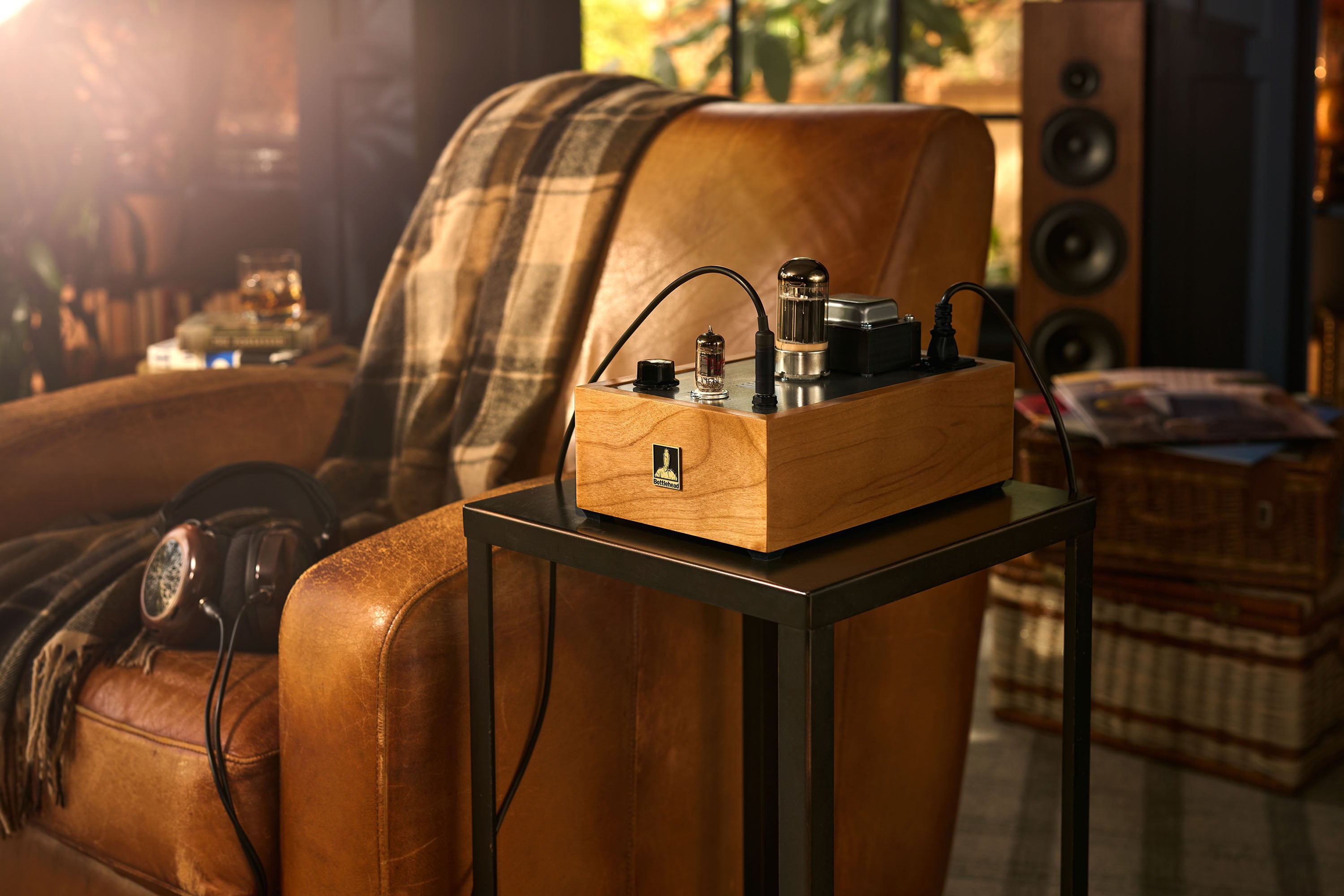Bottlehead Crack headphone amplifier on a side table next to a brown leather armchair in a cozy room.